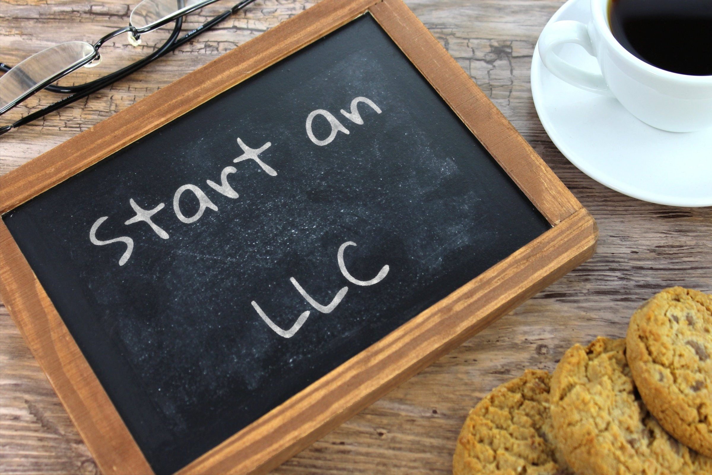 Chalkboard slate with glasses, coffee and cookies template with the words "Start an LLC" written in chalk