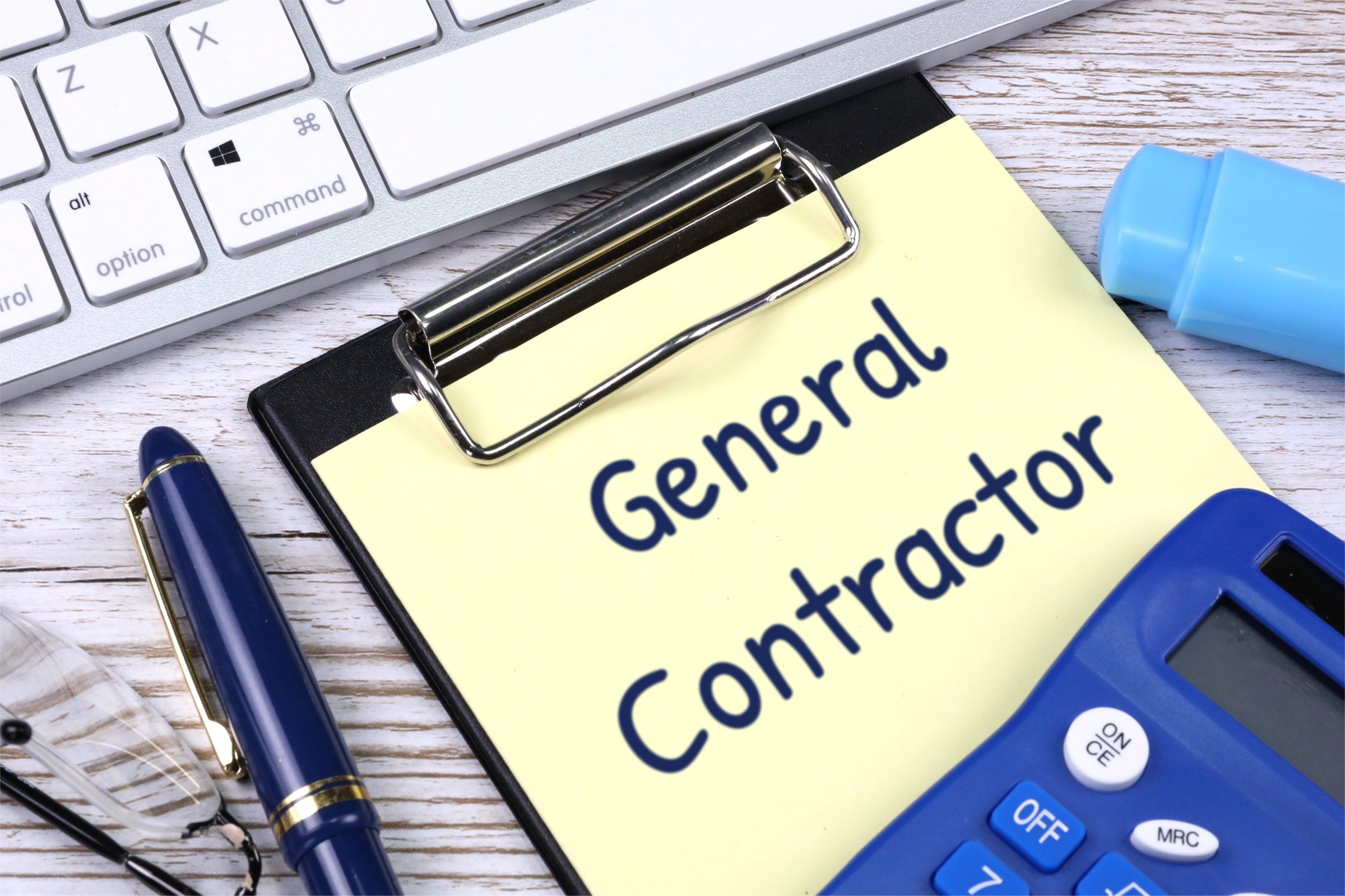 Clipboard with yellow paper, pen and calculator template with the words "General Contractor" printed on the surface