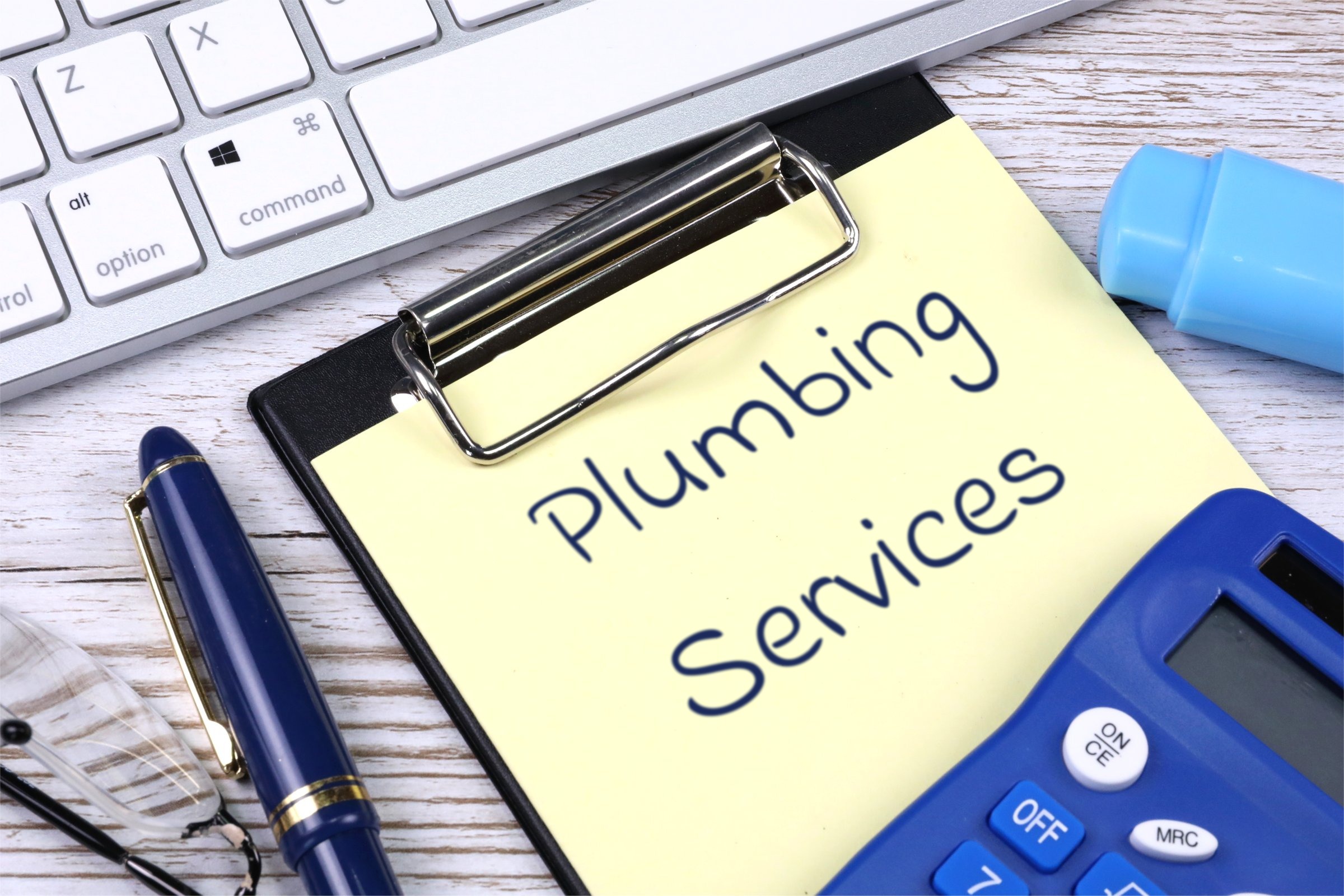 Clipboard with yellow paper, pen and calculator template with the words "Plumbing Services" printed on the surface