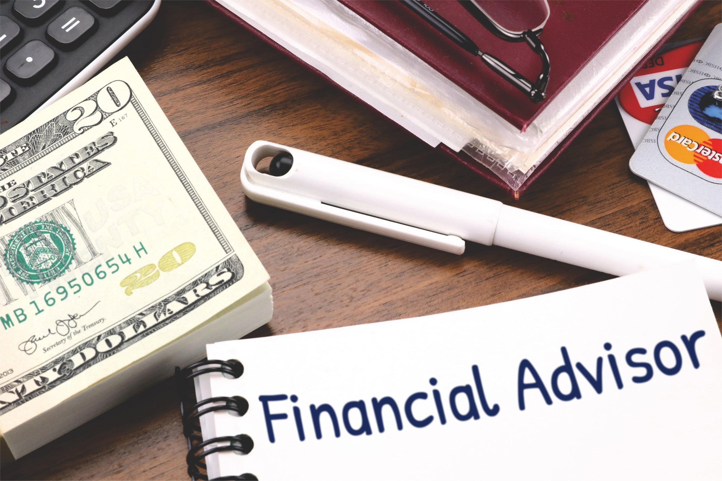 Spiral notepad with a blank page, pen and dollar bills template with the words "Financial Advisor" printed on the surface