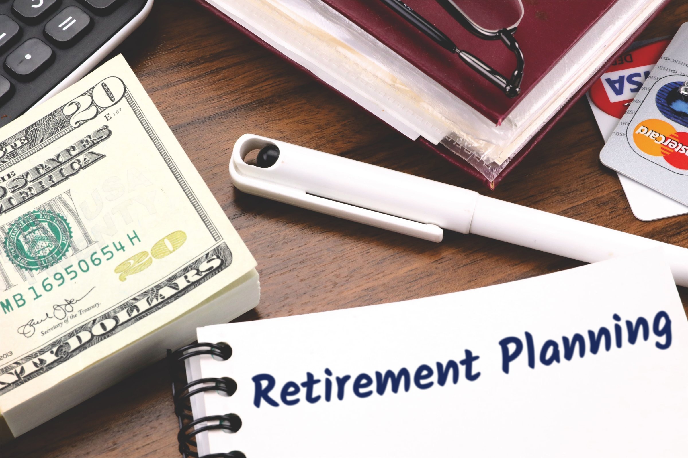 Spiral notepad with a blank page, pen and dollar bills template with the words "Retirement Planning" printed on the surface
