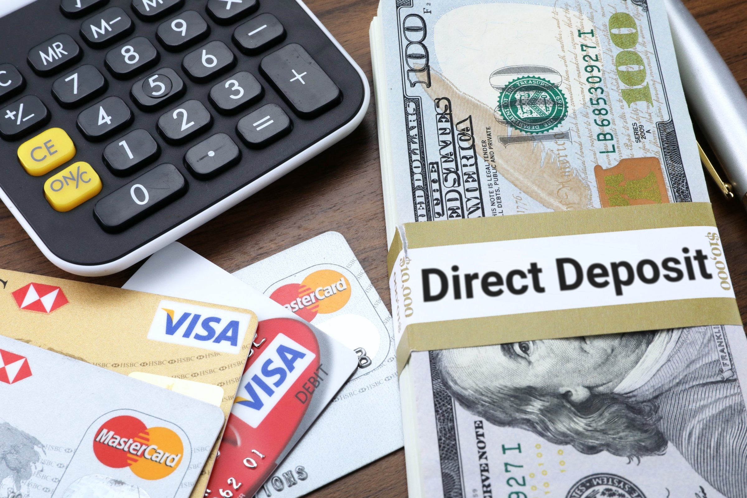 Banded stack of dollar bills with calculator and bank cards template with the words "Direct Deposit" printed on the surface