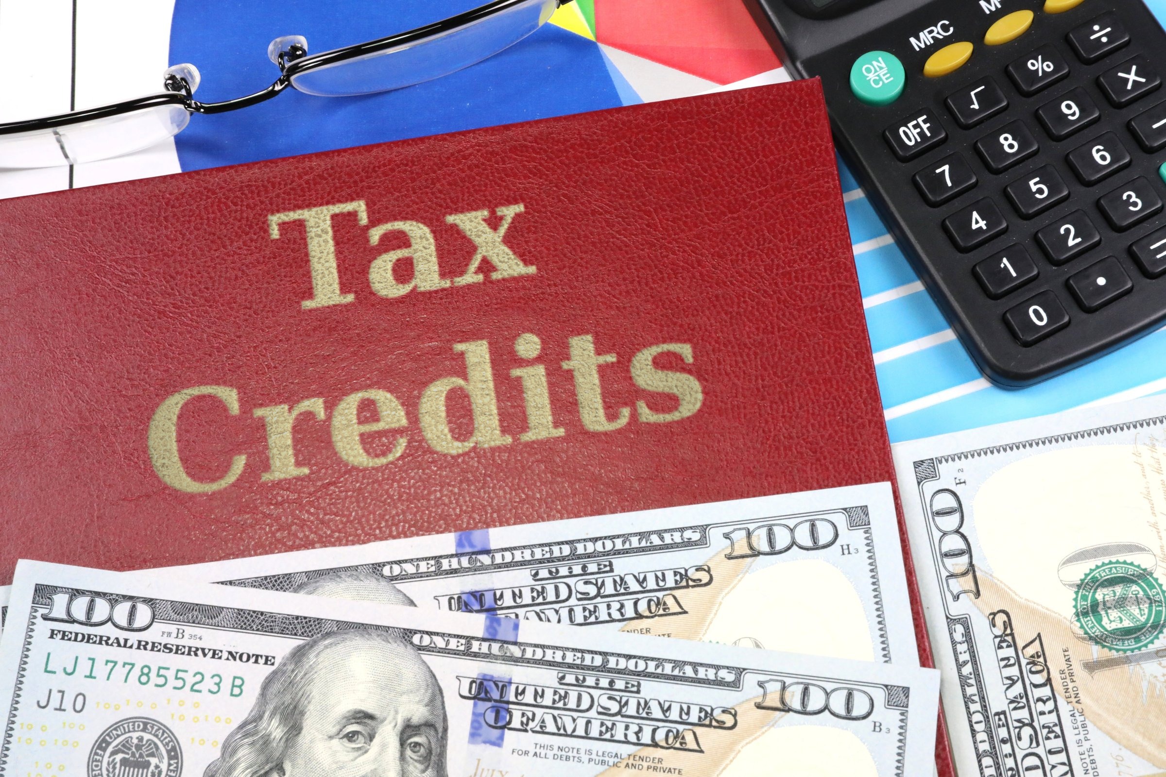 Red leather-look book with dollars and calculator template with the words "Tax Credits" in metallic foil lettering