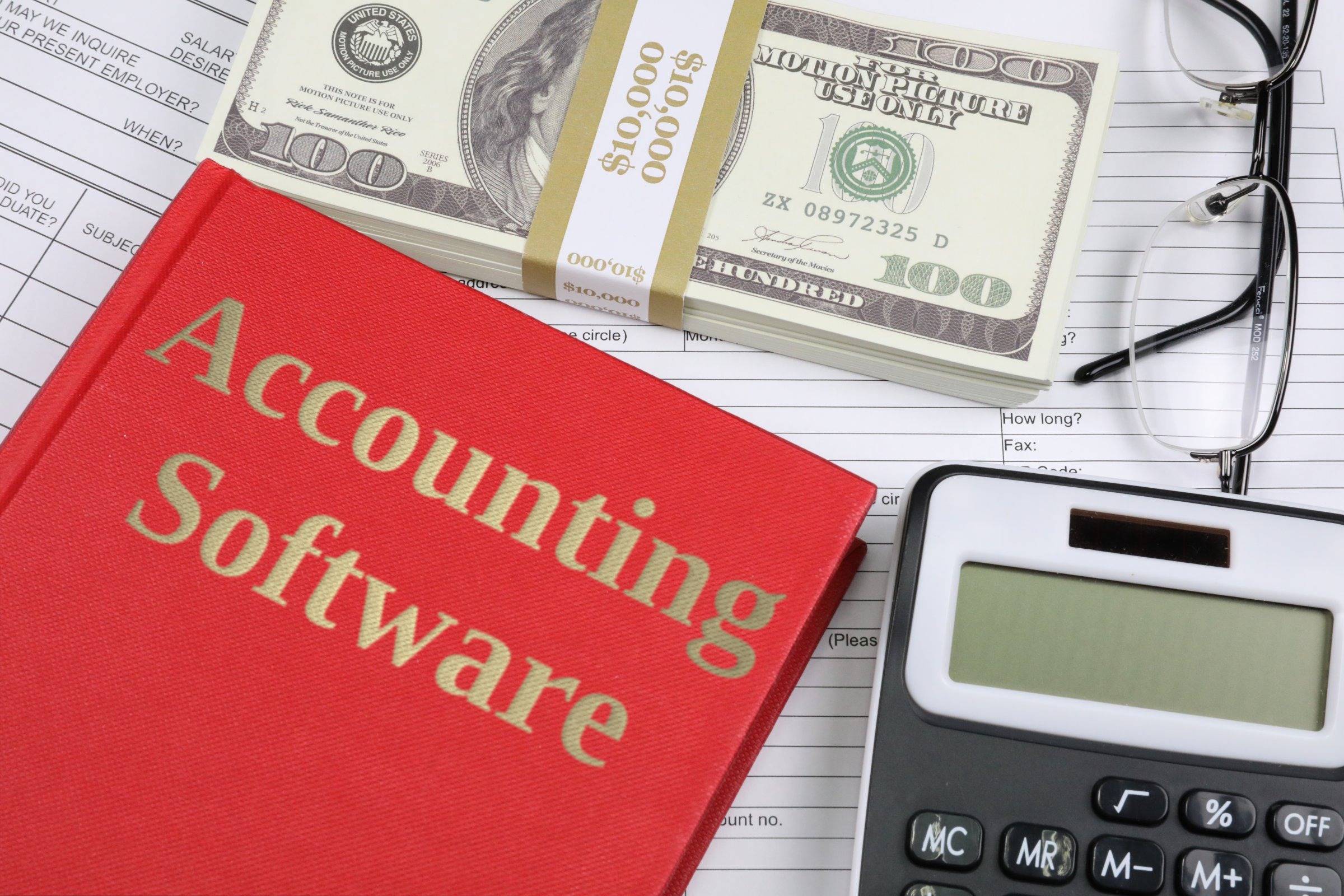 Red hardback book with dollars, glasses and calculator template with the words "Accounting Software" in metallic foil lettering