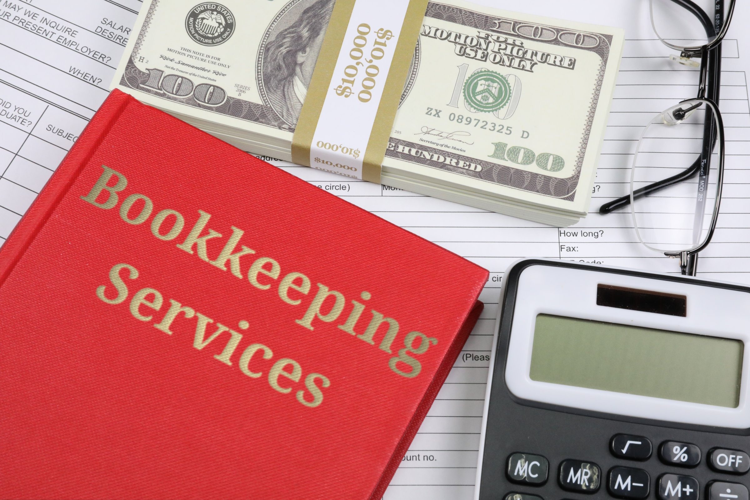 Red hardback book with dollars, glasses and calculator template with the words "Bookkeeping Services" in metallic foil lettering