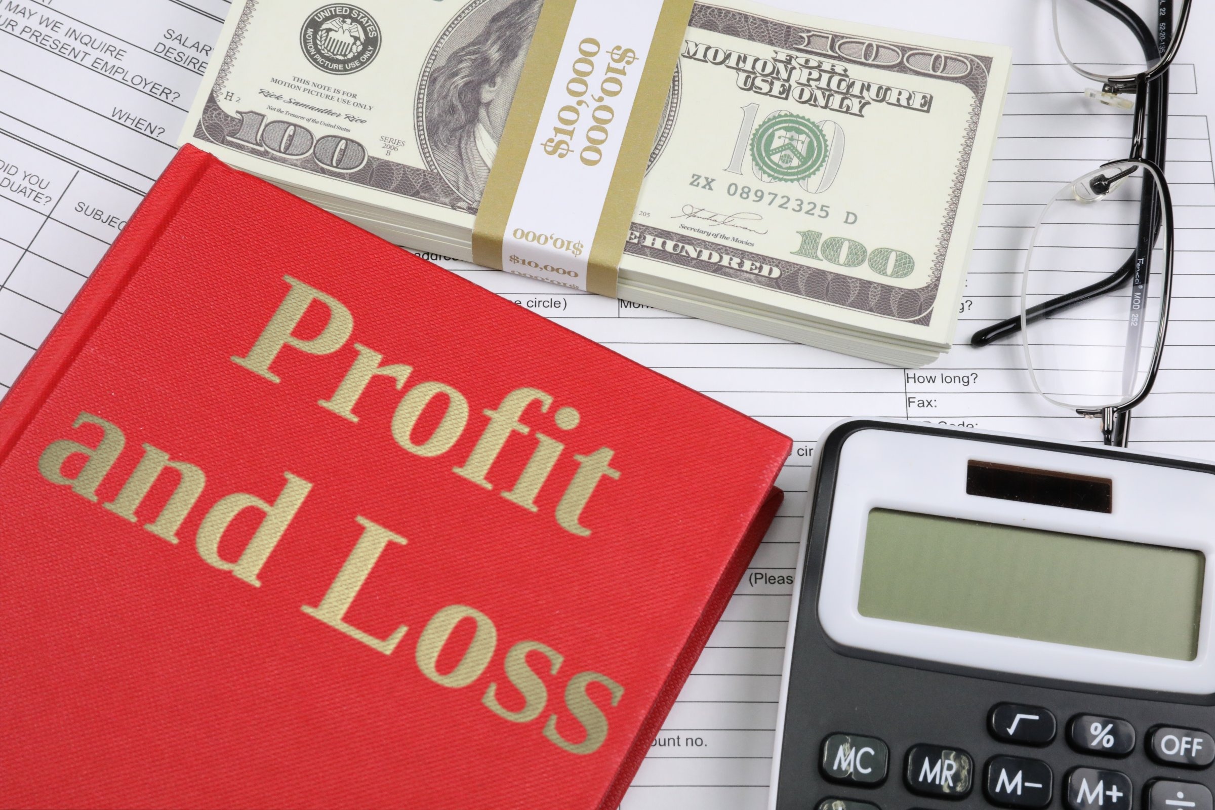 Red hardback book with dollars, glasses and calculator template with the words "Profit and Loss" in metallic foil lettering