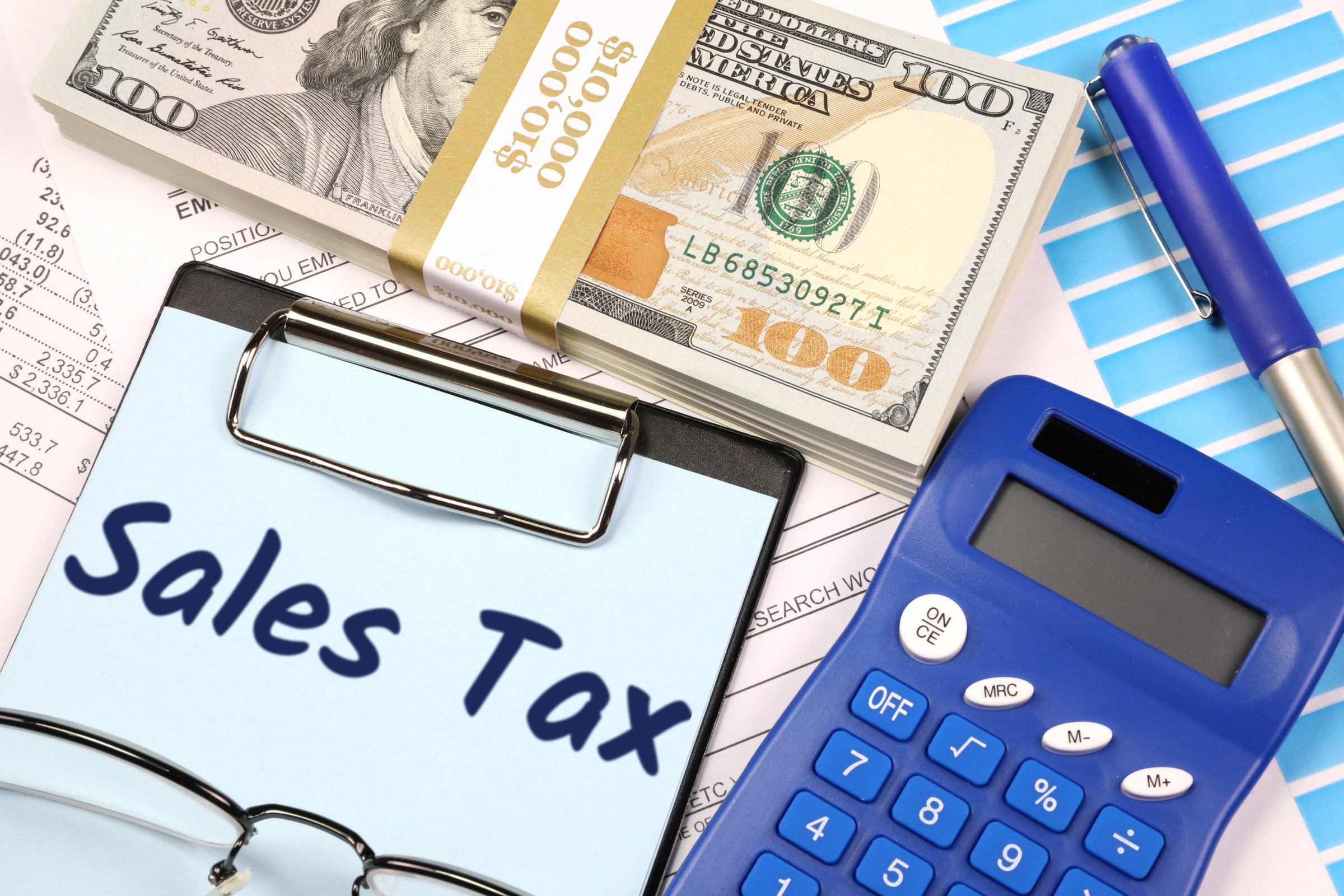 Clipboard with blue paper, dollars and calculator template with the words "Sales Tax" printed on the surface