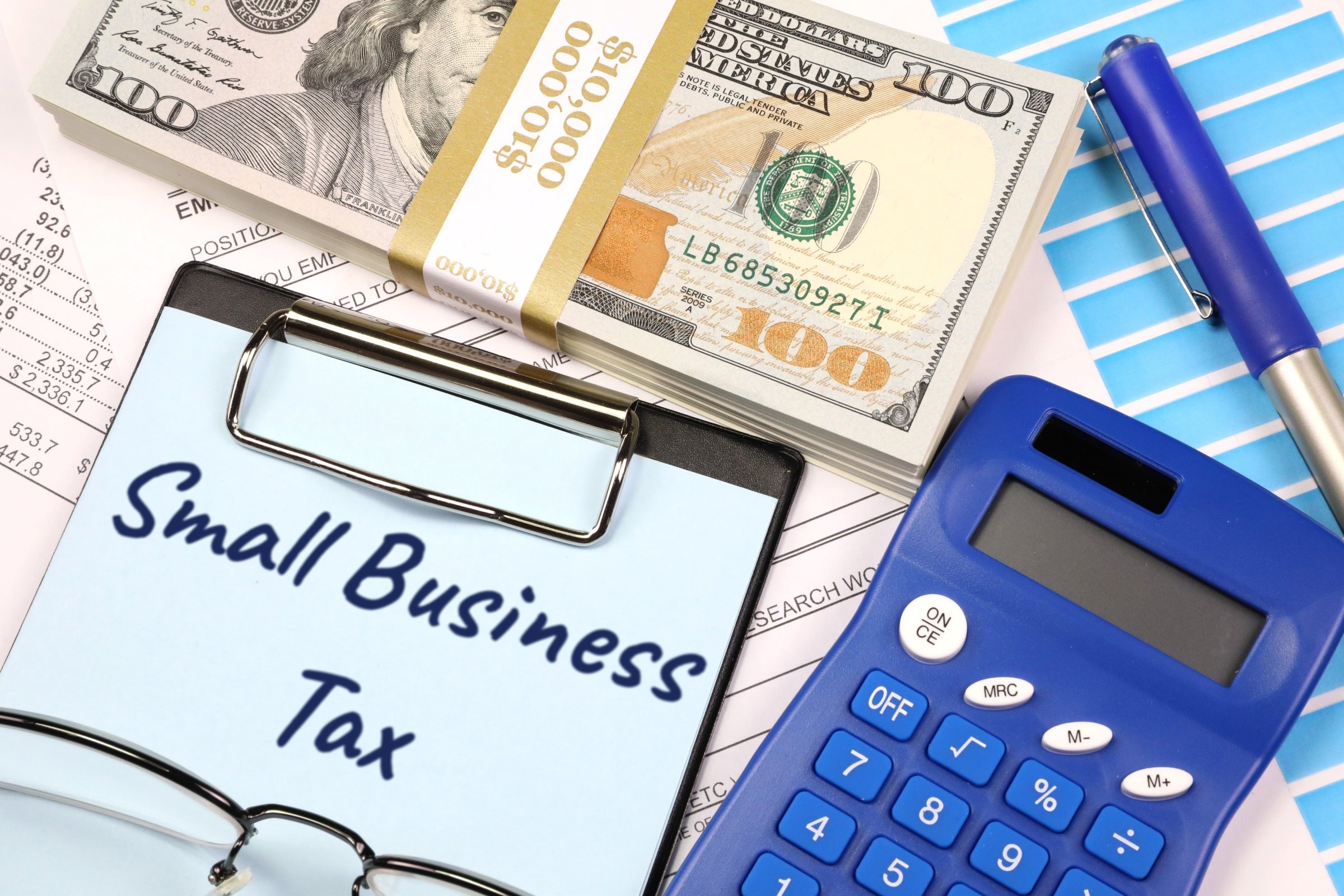 Clipboard with blue paper, dollars and calculator template with the words "Small Business Tax" printed on the surface