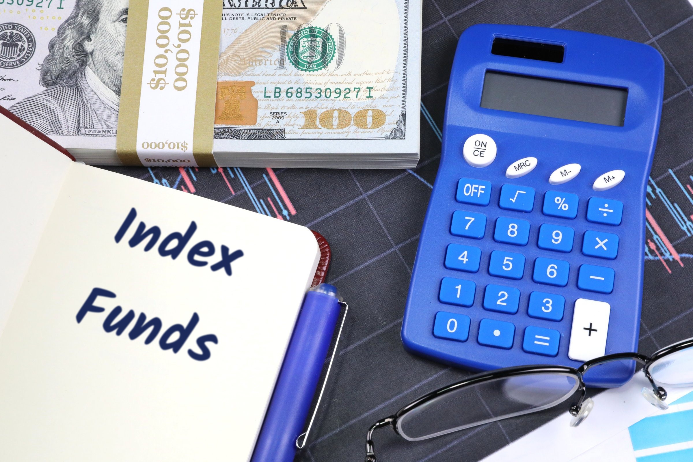 Open notebook with dollars and blue calculator template with the words "Index Funds" printed on the surface