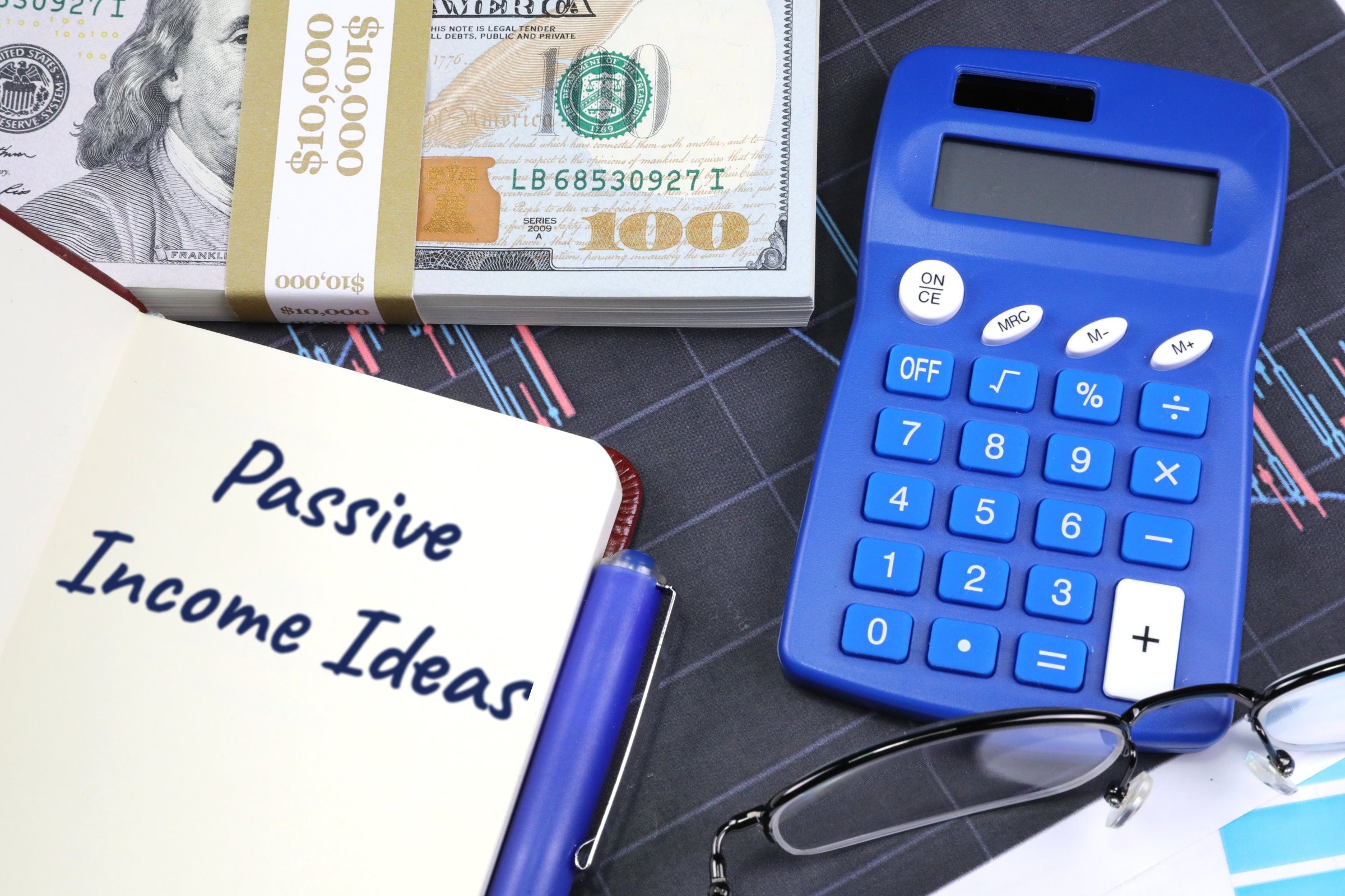 Open notebook with dollars and blue calculator template with the words "Passive Income Ideas" printed on the surface