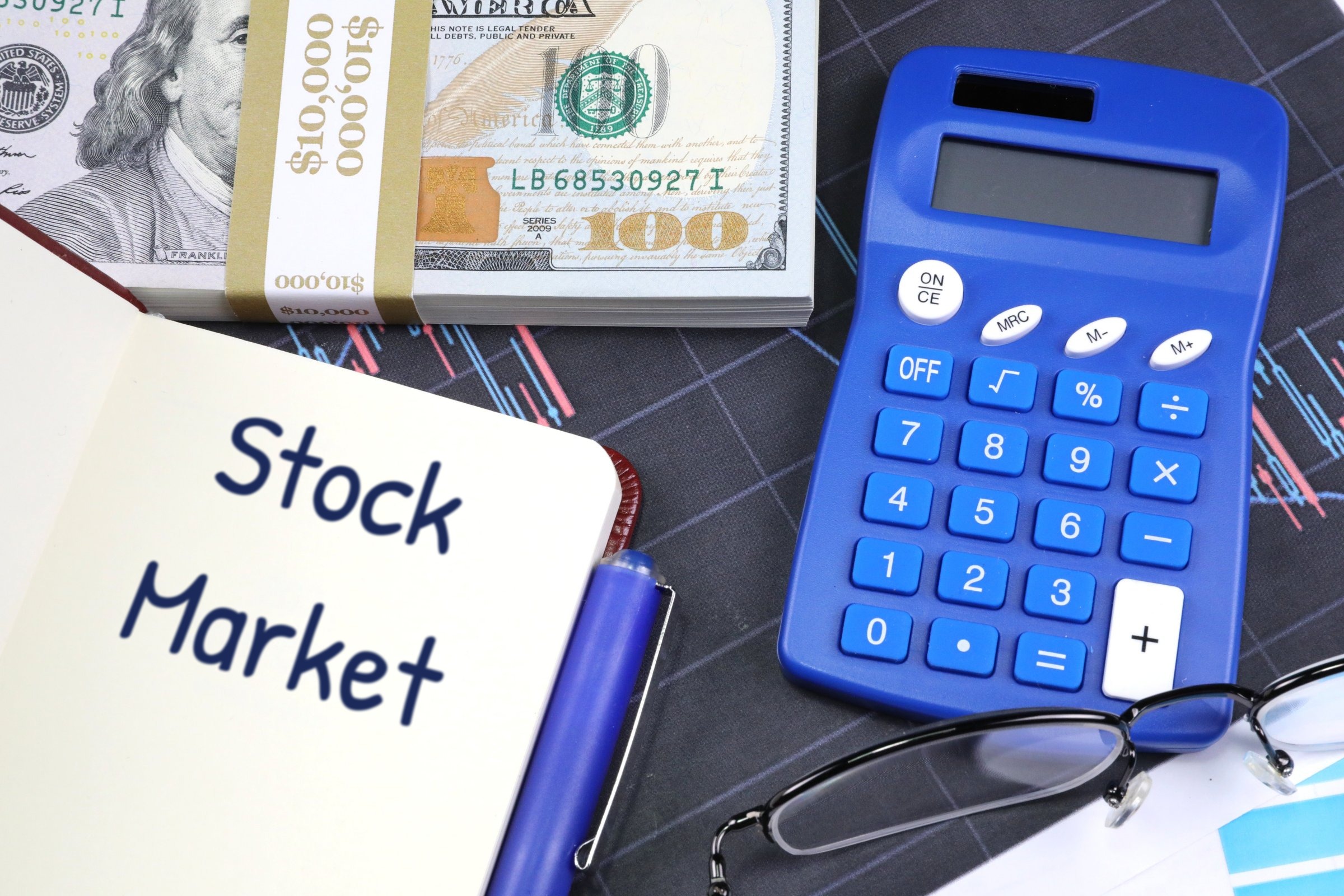 Open notebook with dollars and blue calculator template with the words "Stock Market" printed on the surface