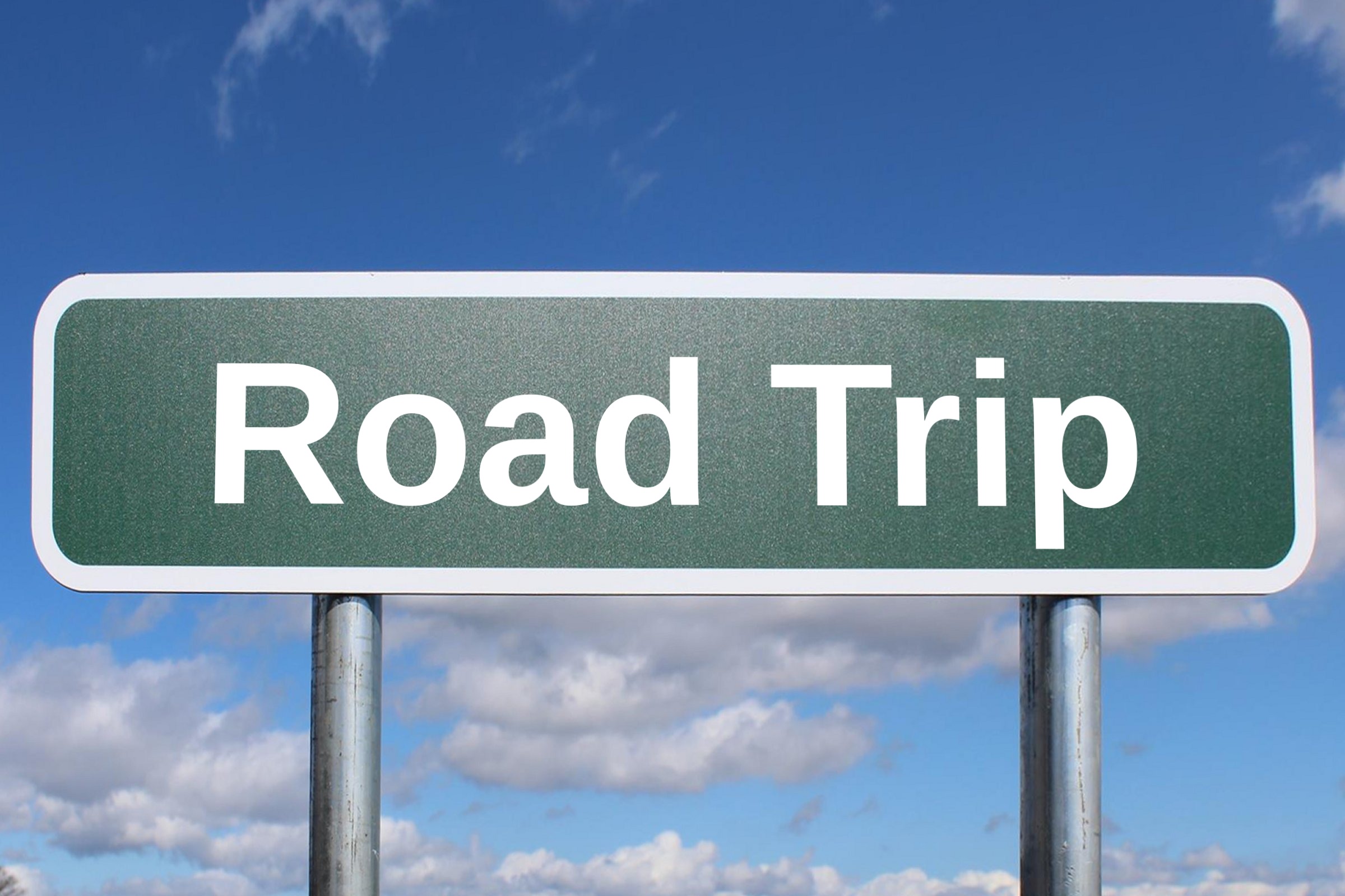 Blank green road sign against a blue sky template with the words "Road Trip" in plain lettering