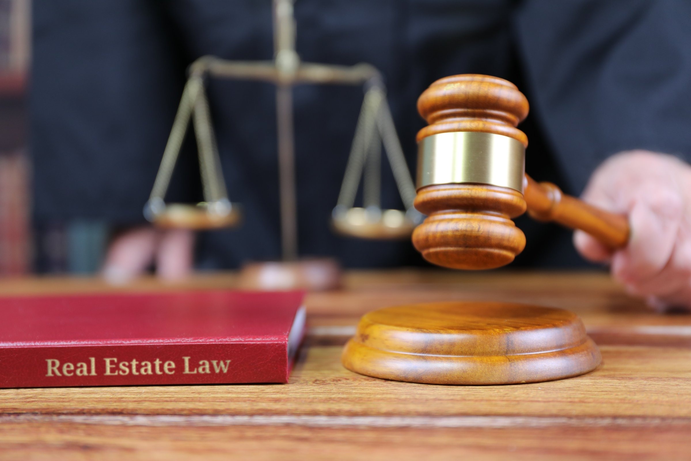 Gavel and scales of justice with a red book template with the words "Real Estate Law" in metallic foil lettering