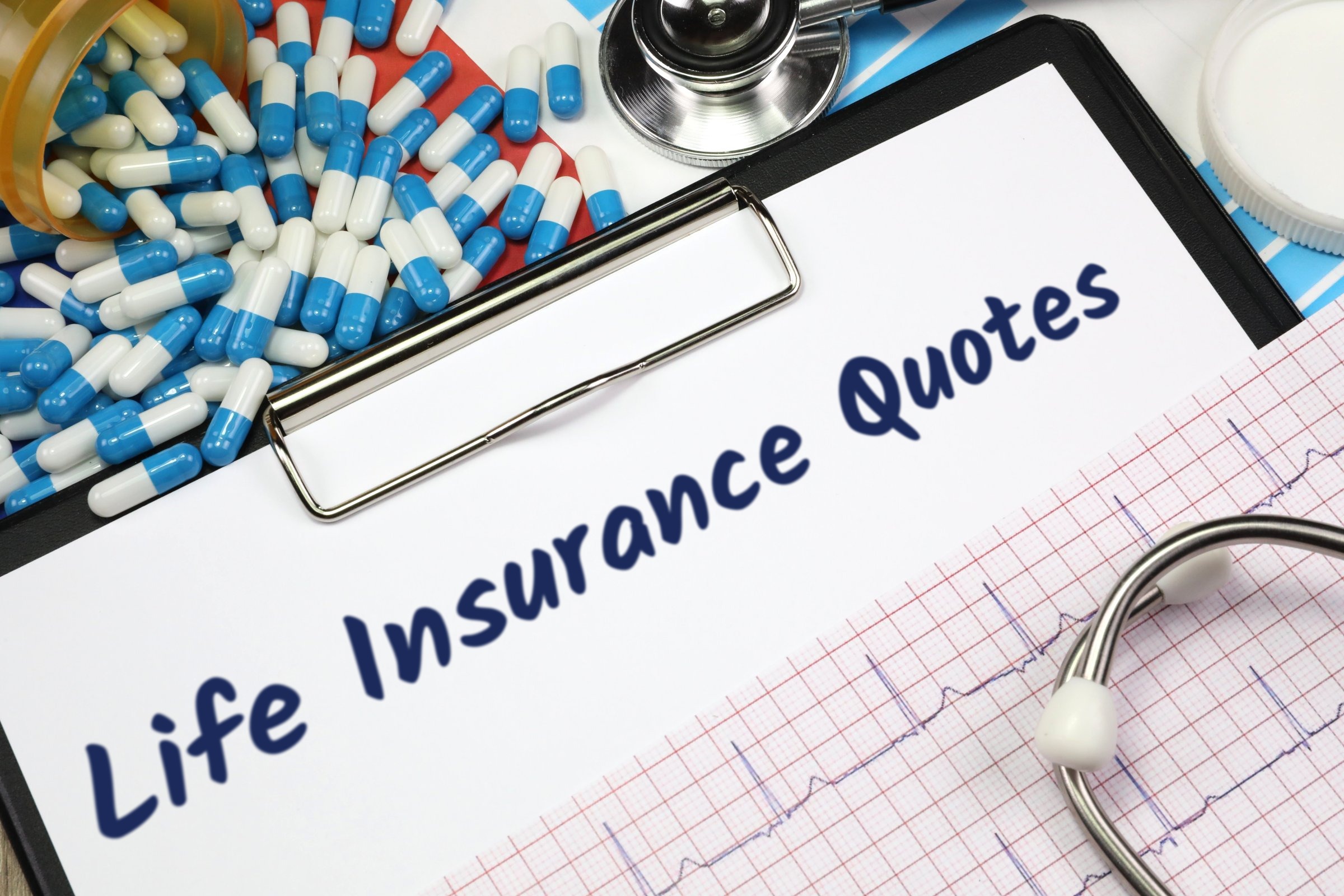 Clipboard with capsules, stethoscope and heart trace template with the words "Life Insurance Quotes" printed on the surface