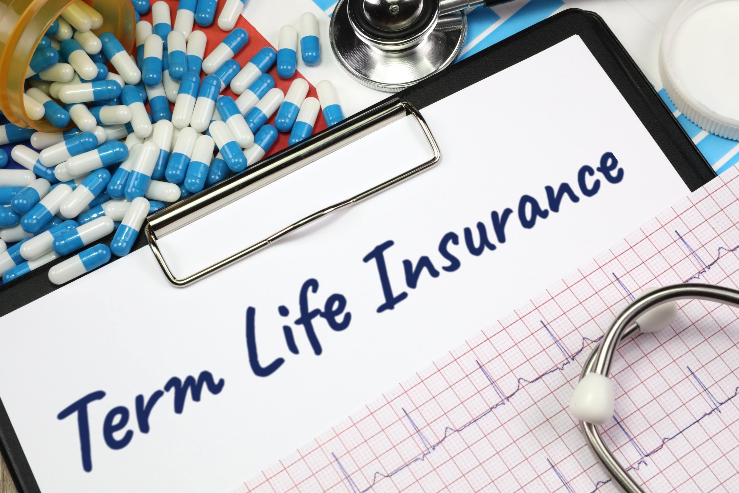 Clipboard with capsules, stethoscope and heart trace template with the words "Term Life Insurance" printed on the surface