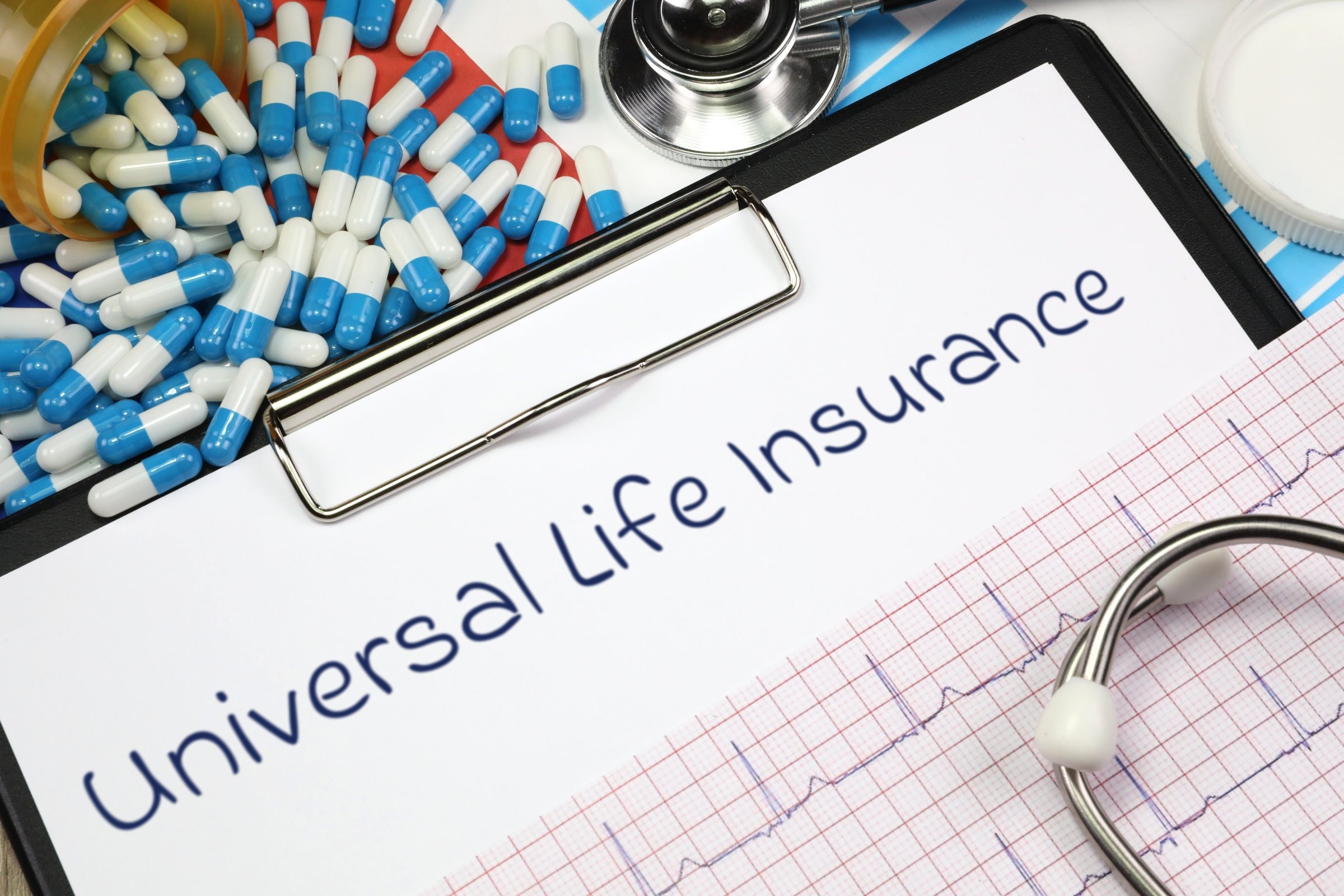 Clipboard with capsules, stethoscope and heart trace template with the words "Universal Life Insurance" printed on the surface