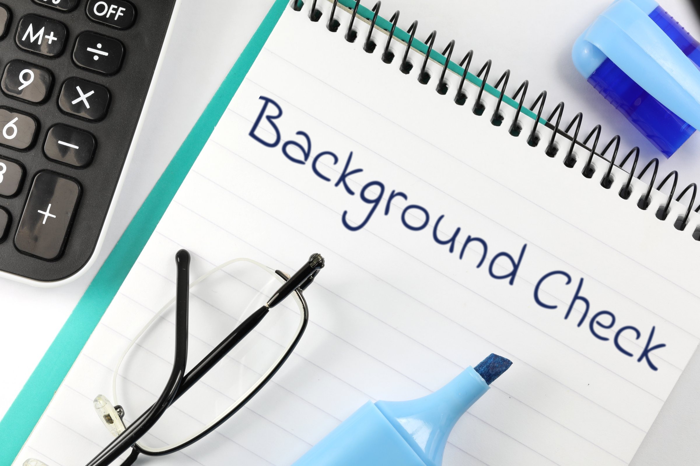 Lined spiral notepad with glasses and highlighter template with the words "Background Check" printed on the surface