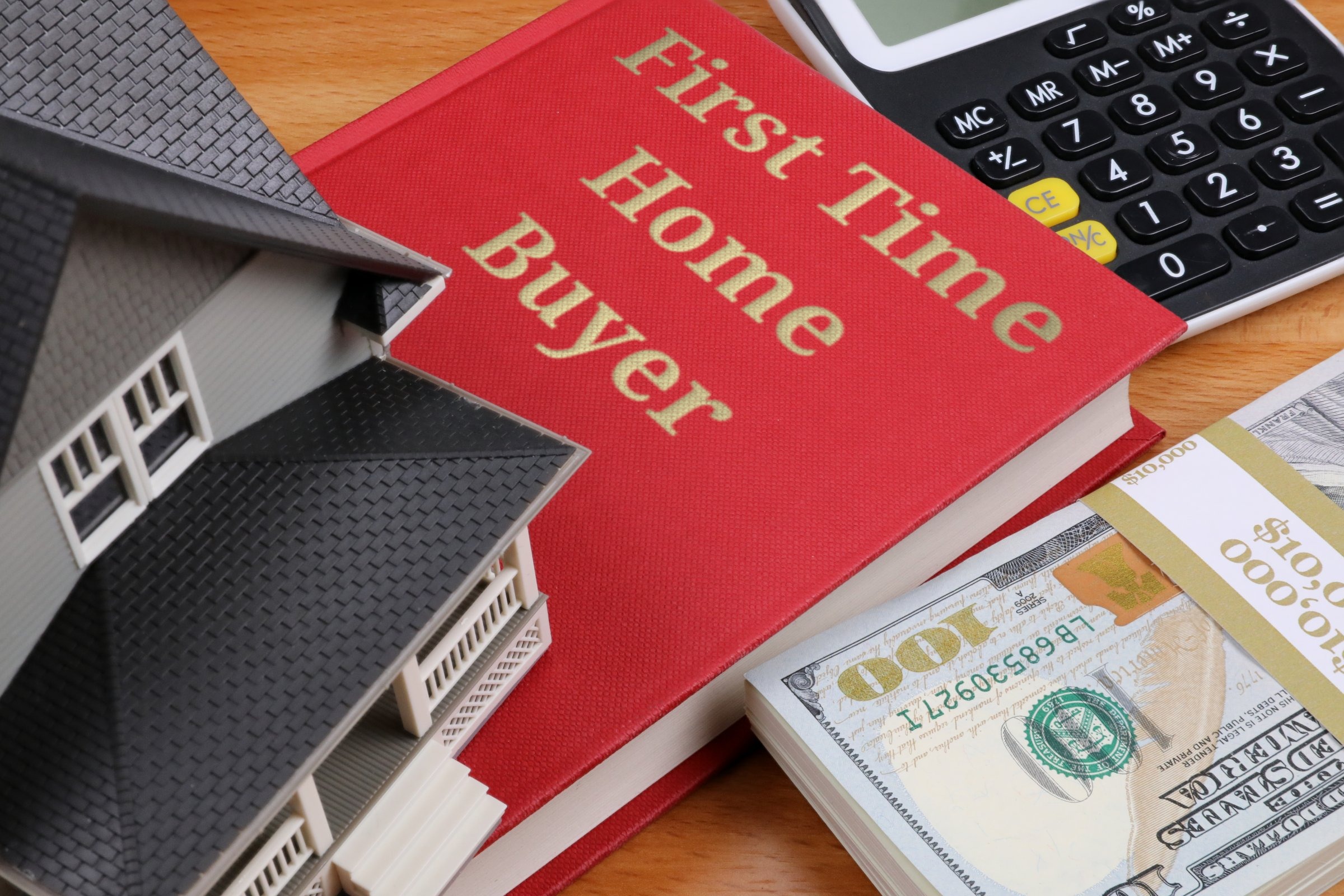 Red book with a model house and dollars template with the words "First Time Home Buyer" in metallic foil lettering