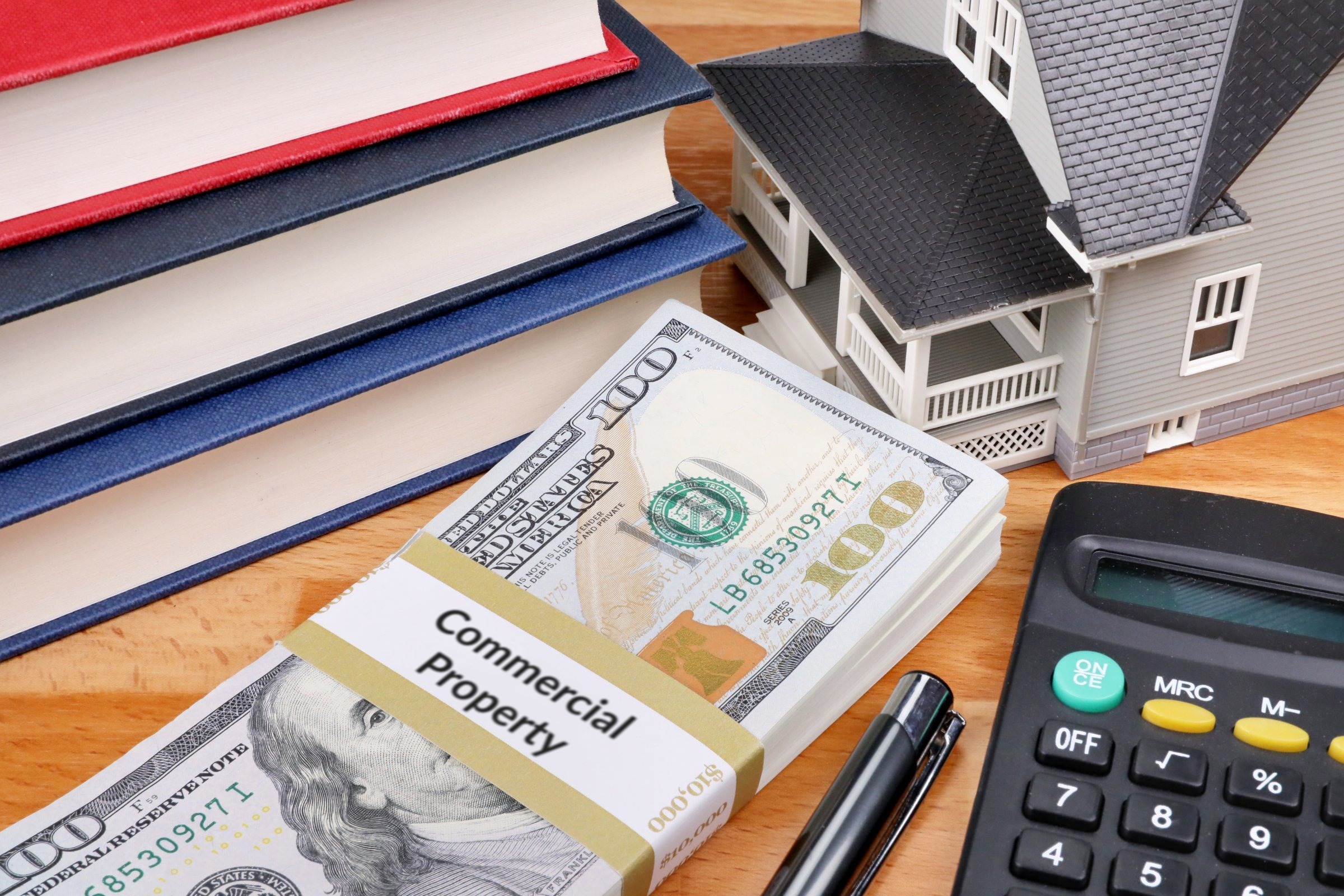 Stack of dollars with a banded label, model house and books template with the words "Commercial Property" printed on the surface