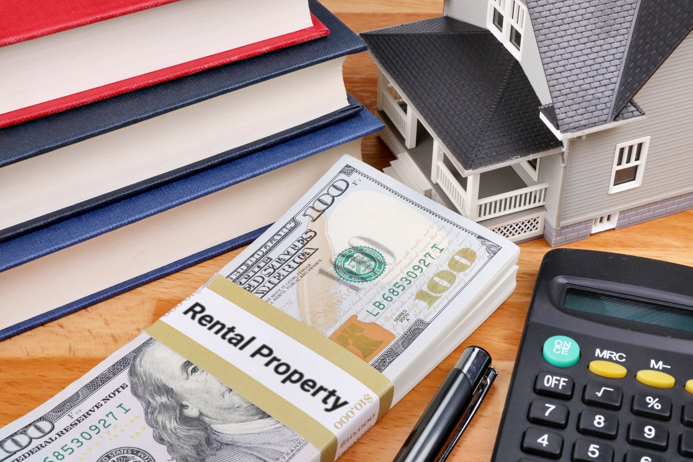 Stack of dollars with a banded label, model house and books template with the words "Rental Property" printed on the surface
